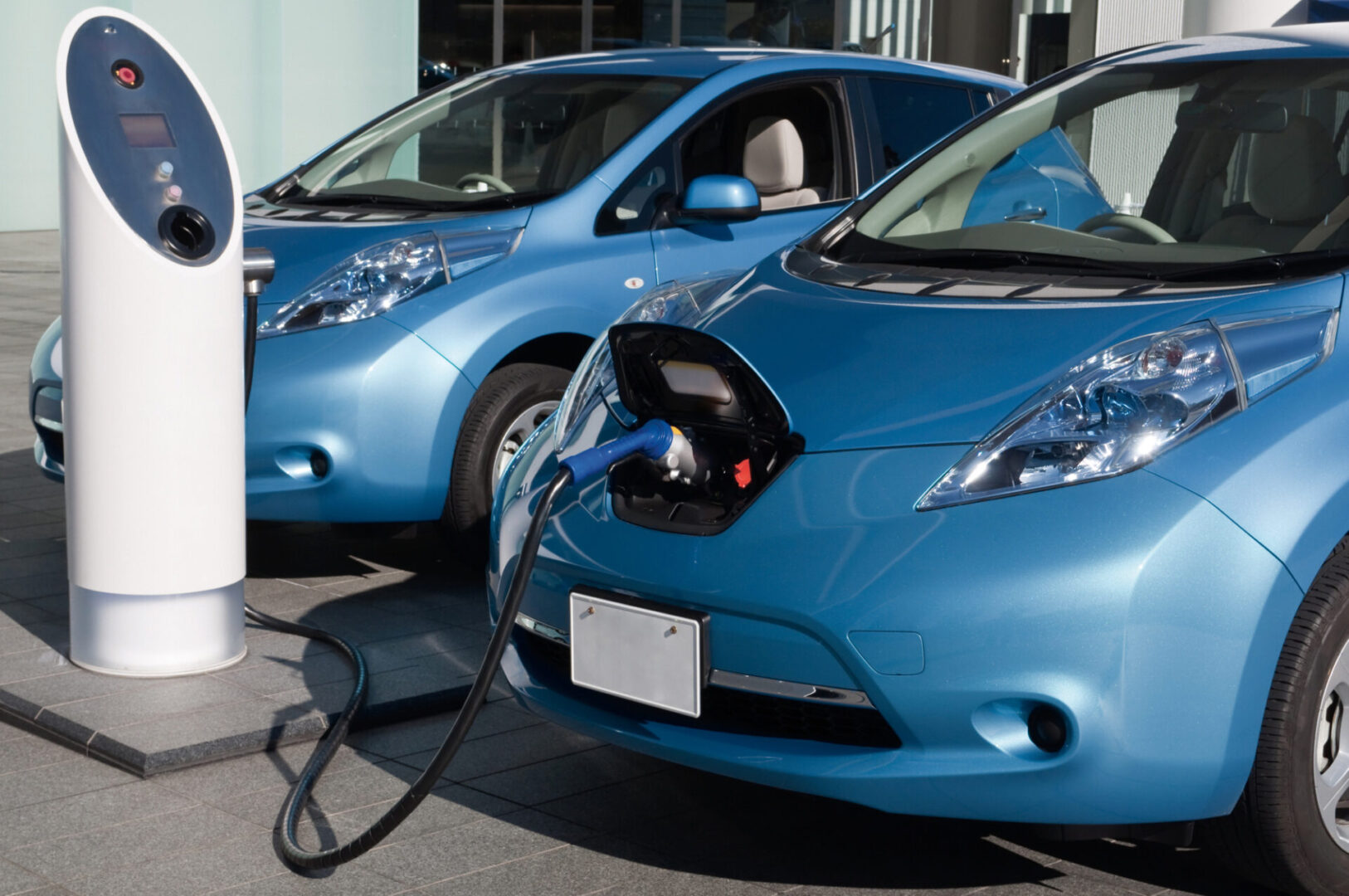 Two blue electric cars parked side by side, with one car connected to a charging station by a cable.