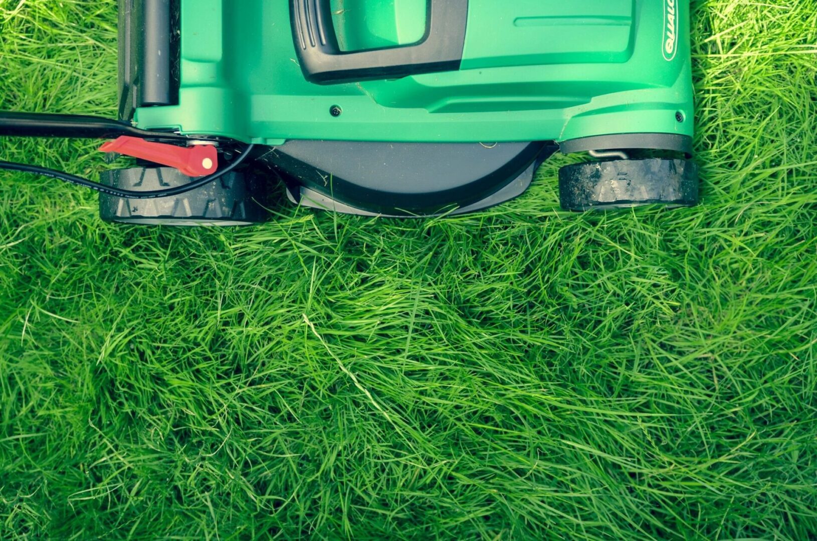 Close-up of a green lawn mower on grass, showing the mower's wheels and handle on a freshly cut lawn.